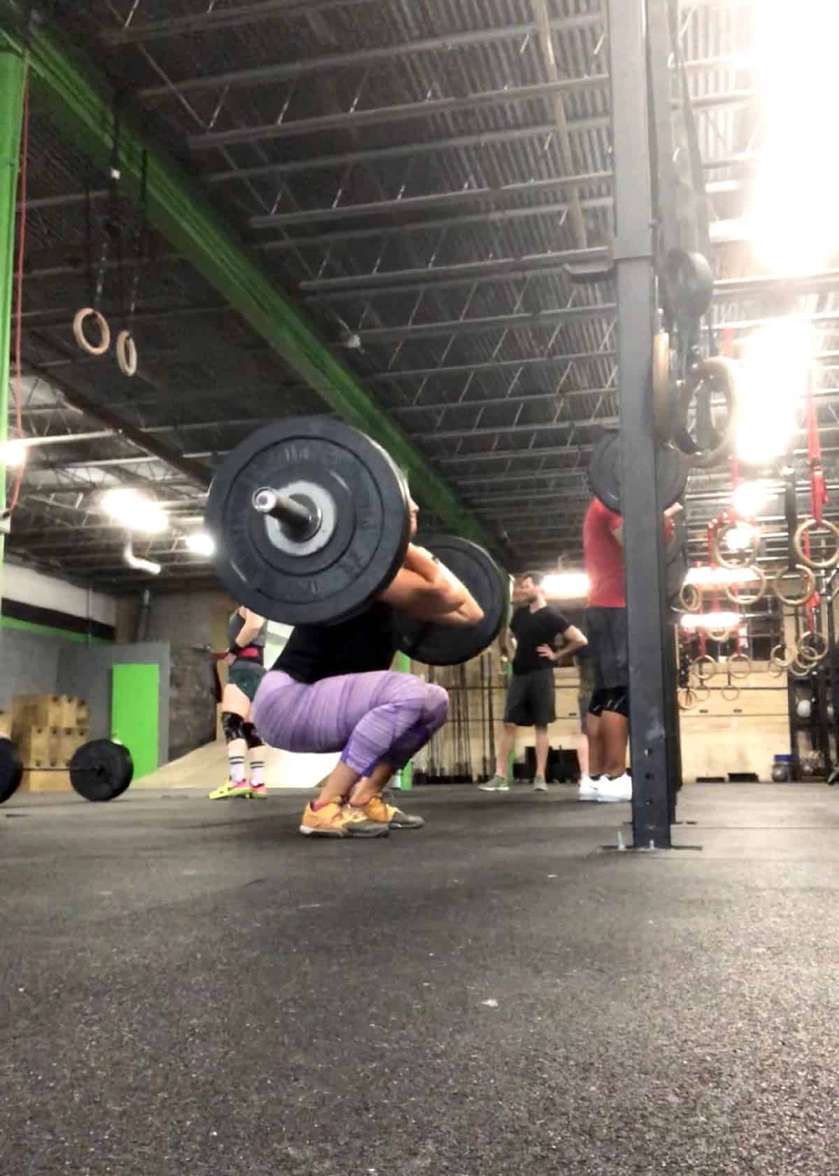 Girl in the bottom of a squat doing front squats with a loaded barbell