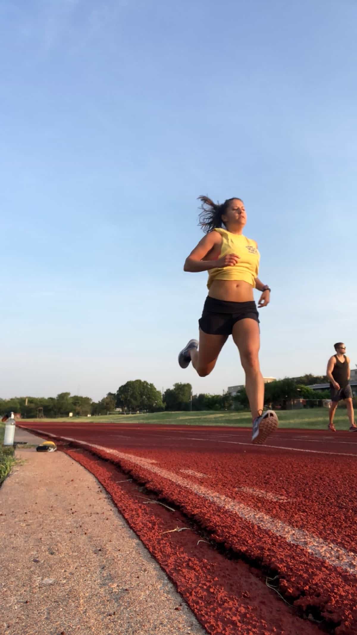 Girl in shorts and a tank doing sprints on a track