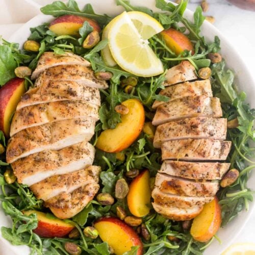 Large white bowl filled with a Peach and Pistachio Salad with Grilled Chicken on top of a white linen