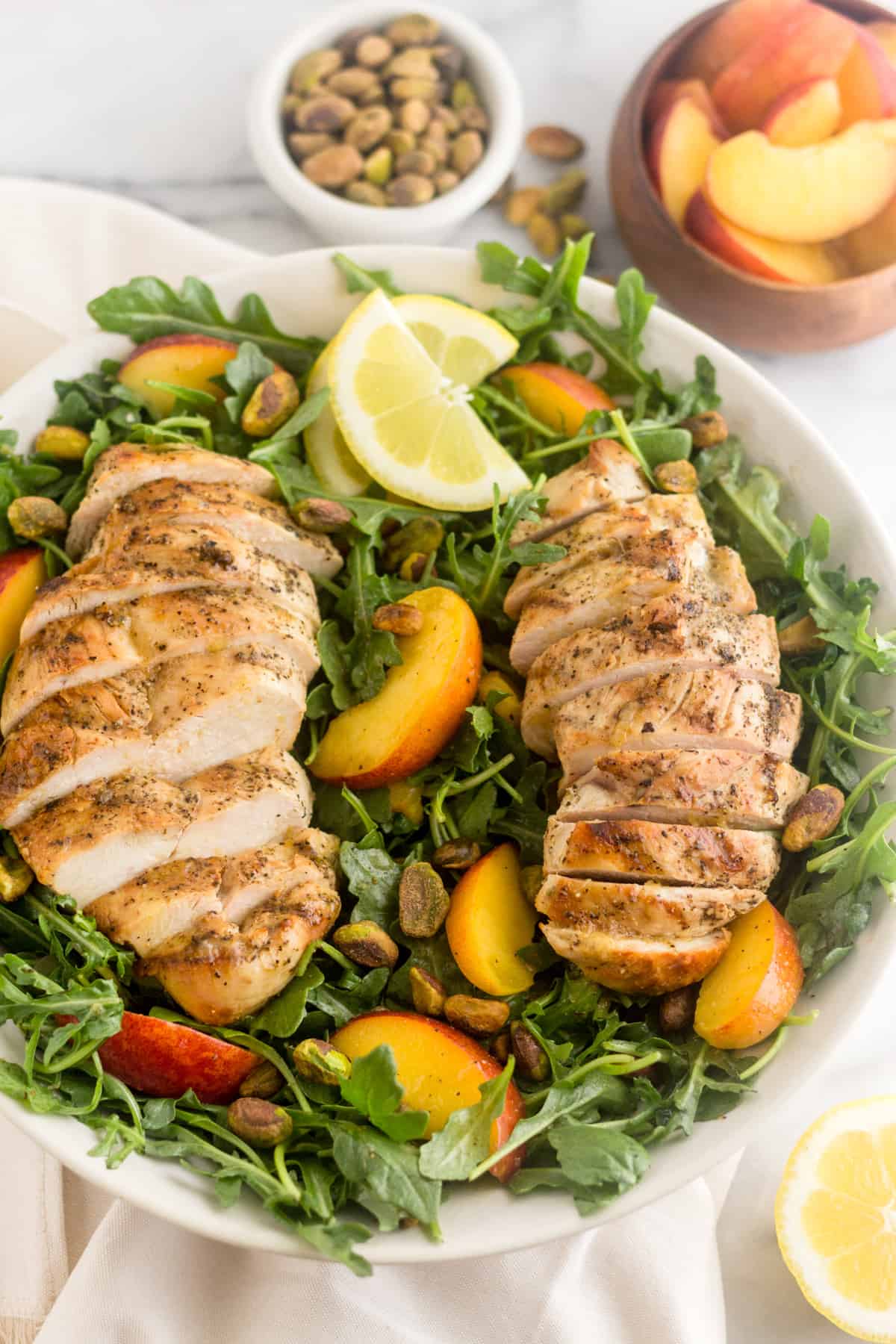 Large Peach and Pistachio Salad with Grilled Chicken garnished with lemon wedges