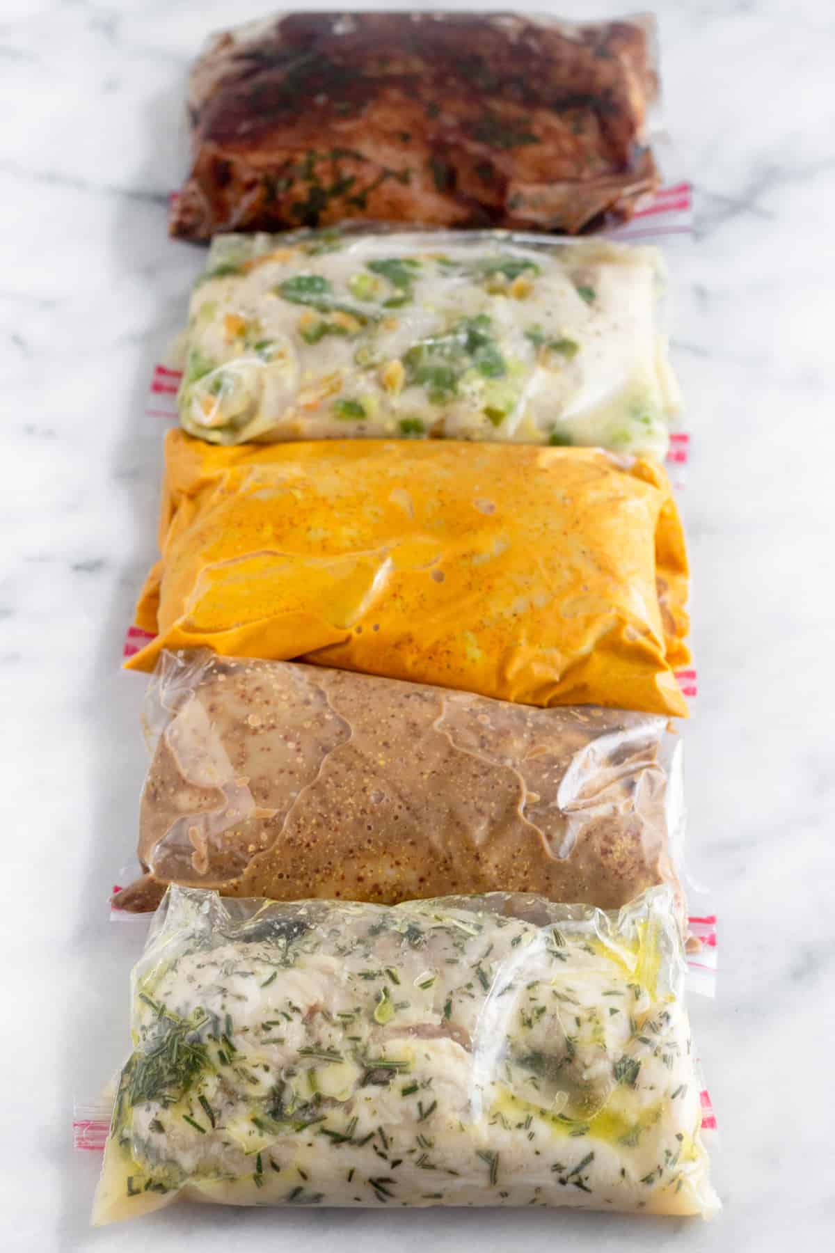 5 plastic bags on white counter top filled with Whole30 Chicken Marinade 5 different ways.