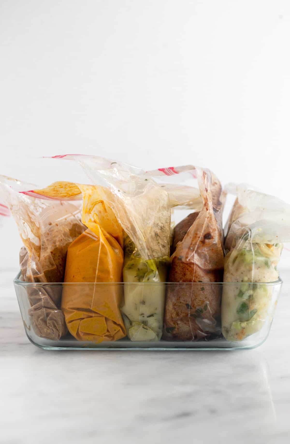 Glass baking dish on a white counter with 5 bags of chicken and marinade in it