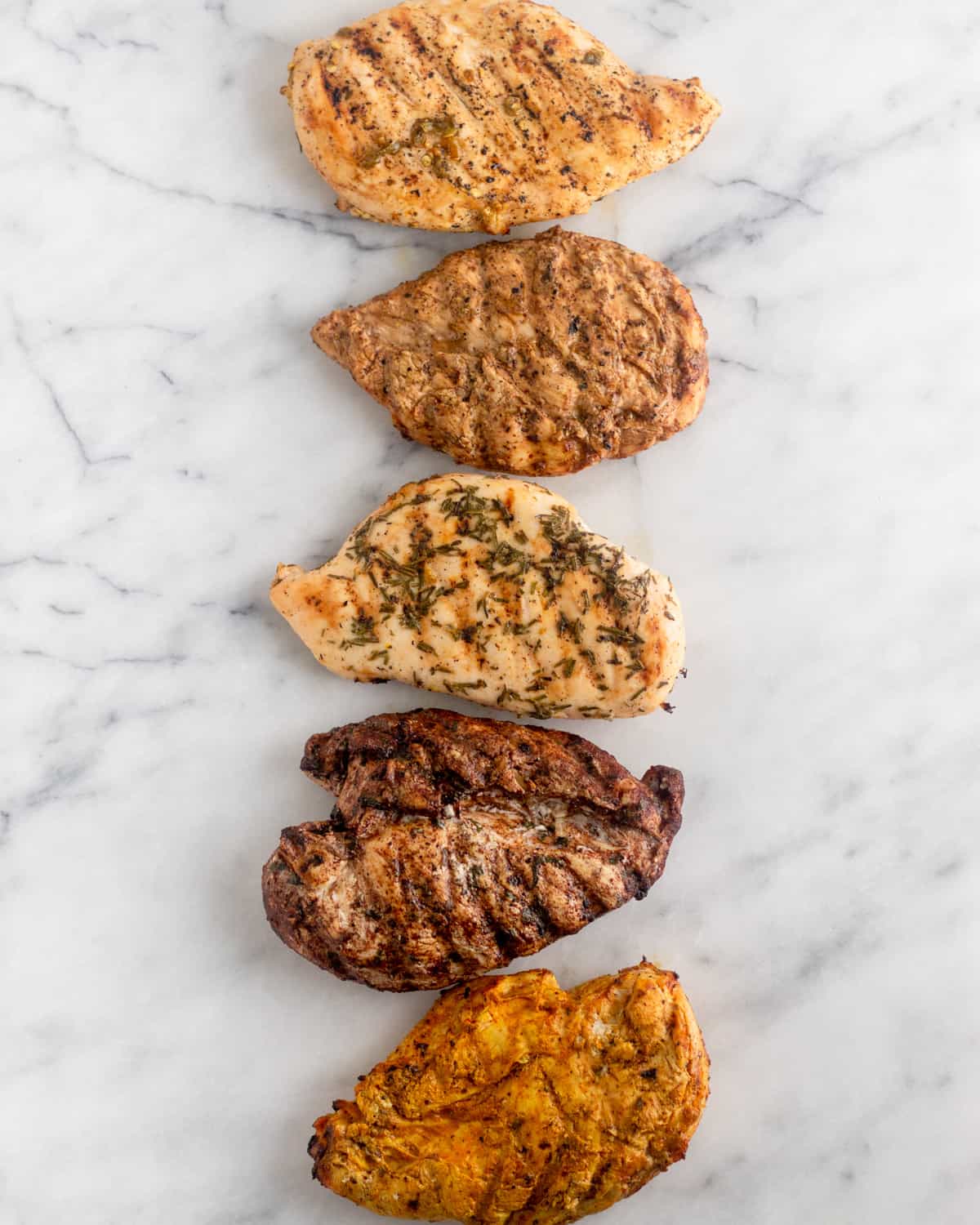 White counter with 5 pieces of grilled chicken breast on them, each with a different whole30 chicken marinade