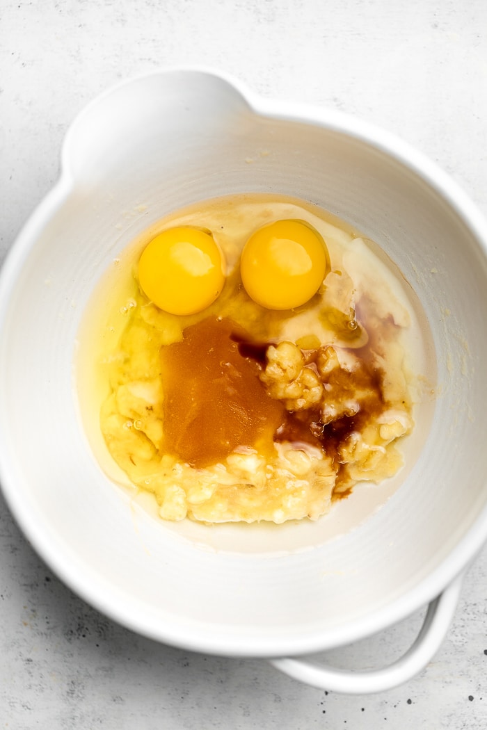 Large bowl with mashed banana, two eggs, honey, coconut oil, and vanilla extract in it.