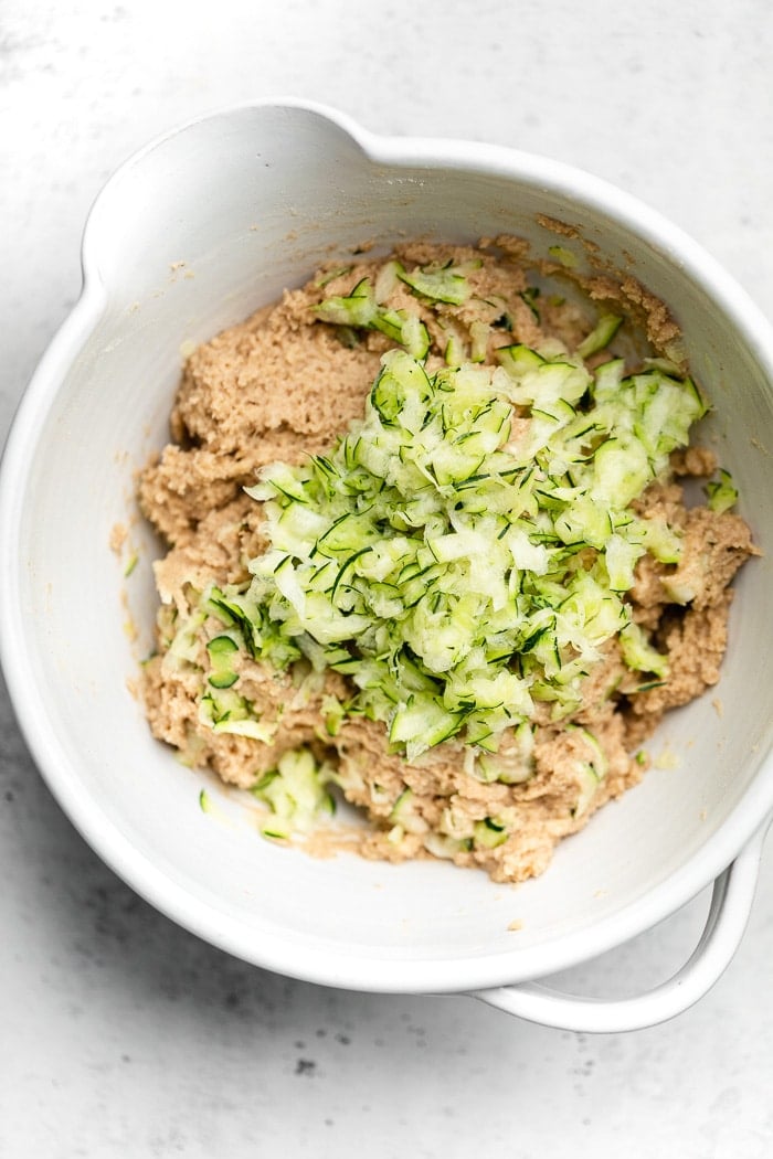 Large bowl with the batter of zucchini a with shredded zucchini on top.