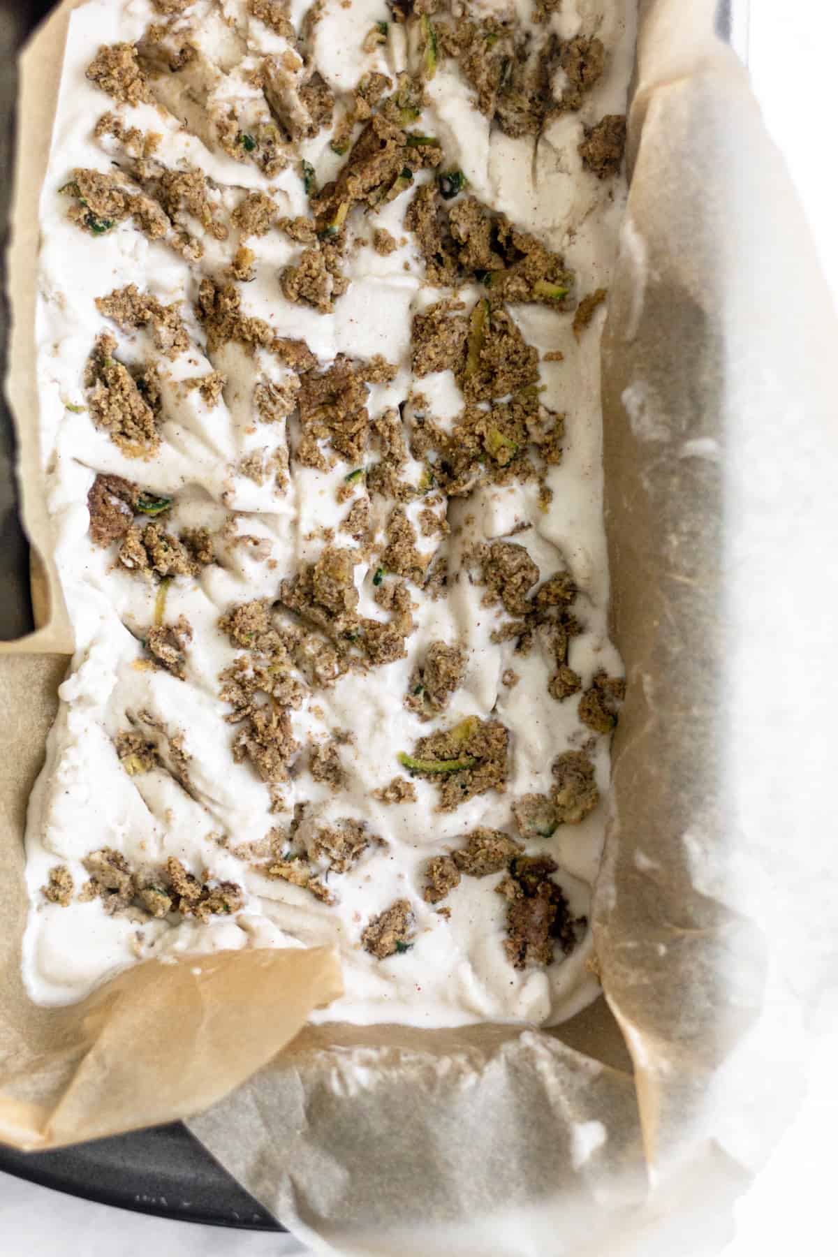 Dairy Free Paleo Zucchini Bread Ice Cream in a loaf pan with big chucks of zucchini bread in it before it is frozen