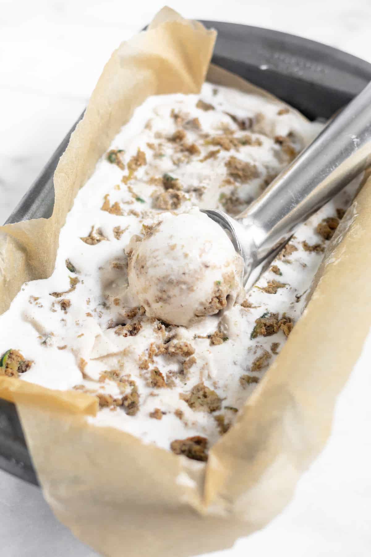 Dairy Free Paleo Zucchini Bread Ice Cream in a small bread pan with an ice cream scoop and a scoop of ice cream in it