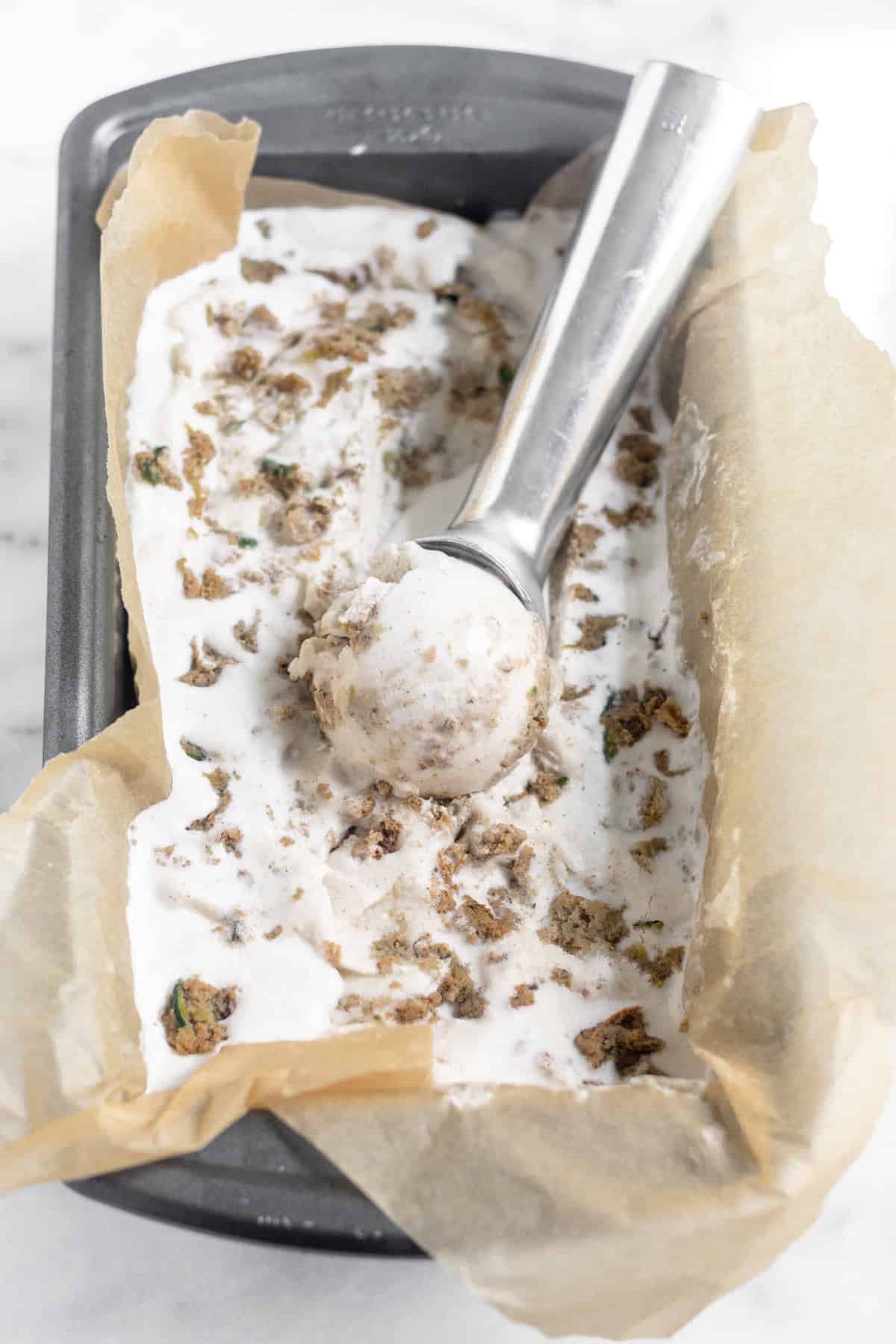 A full loaf pan of Dairy Free Paleo Zucchini Bread Ice Cream with a silver ice cream scoop sitting on top of it