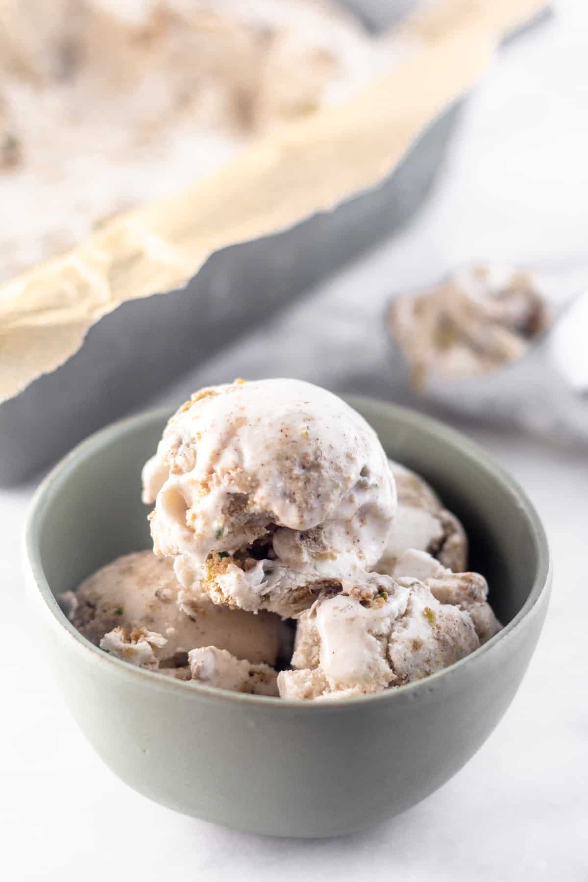 Bowl of paleo zucchini bread ice cream with an ice cream scoop filled and a loaf pan filled with ice cream behind it