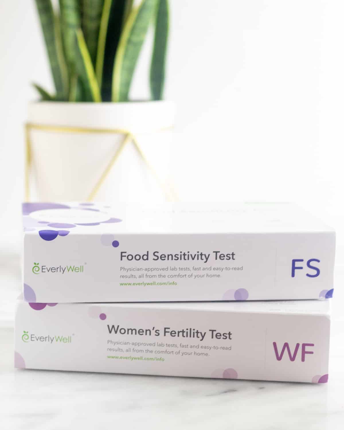 Two boxes of EverlyWell tests - one food sensitivity test and one women's fertility test - on a white counter with a plant behind it