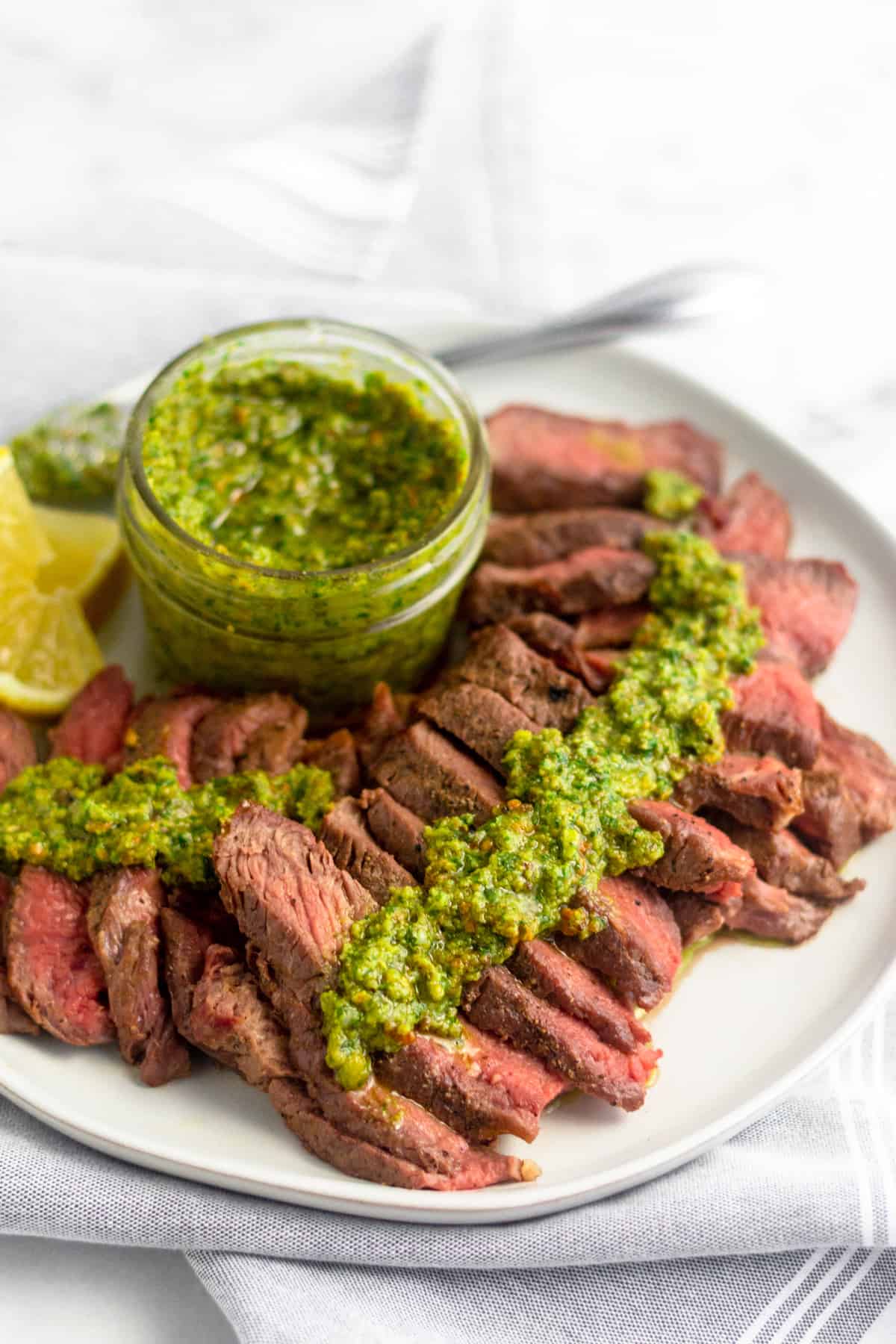 Cut up grilled steak with pistachio pesto on it on a white plate