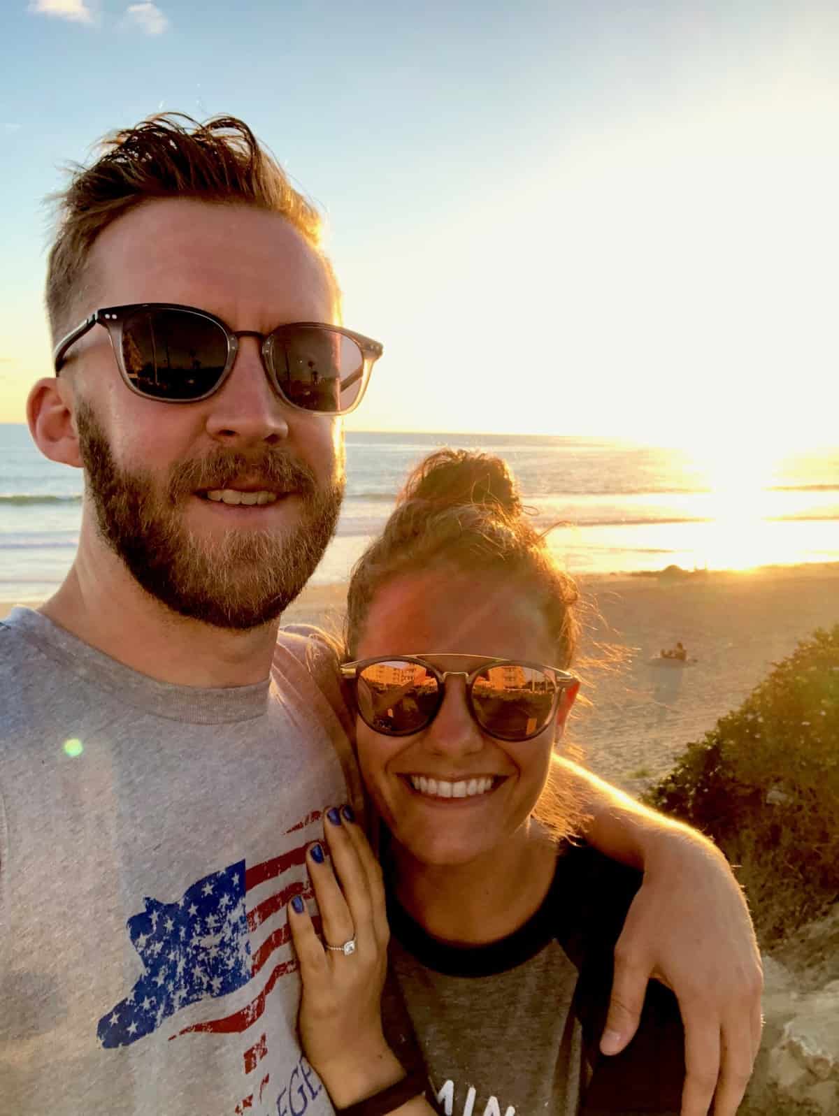 Guys and girl taking a selfie with the sun setting on the ocean behind them