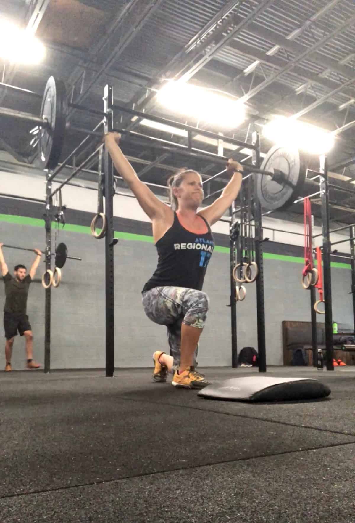 Girl in a CrossFit gym doing an weighted overhead lunge with a barbell