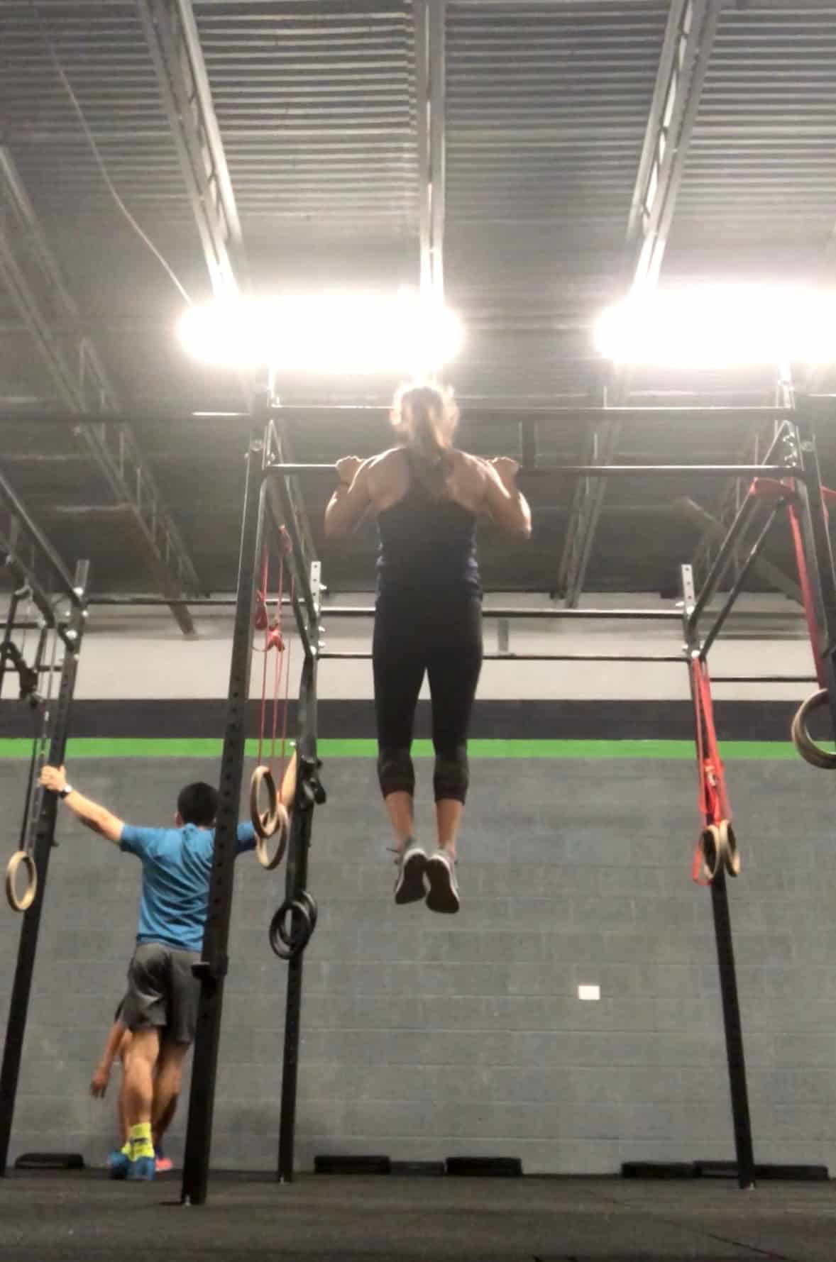 Girl doing a strict pull-up from a pull-up rig in a CrossFit gym
