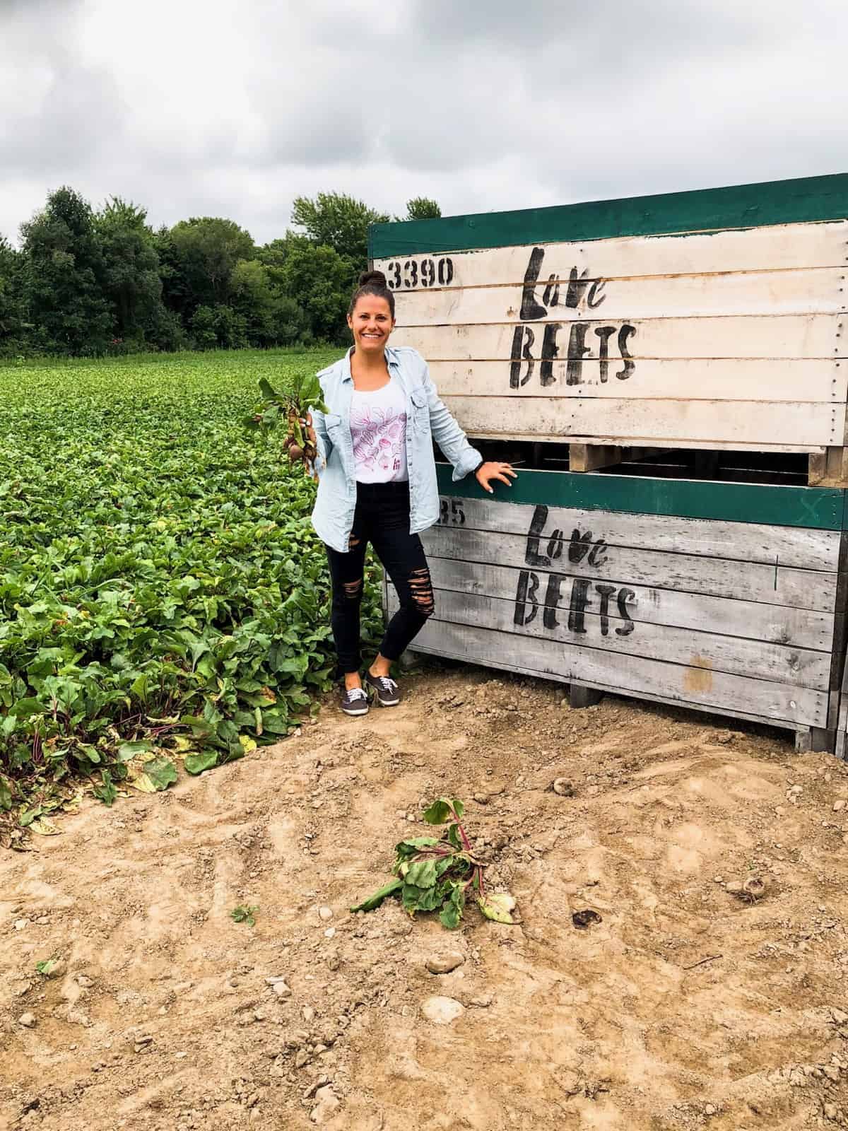 Girl on a beet farm holding 3 beets in front of 2 large wooden crates that say Love Beets