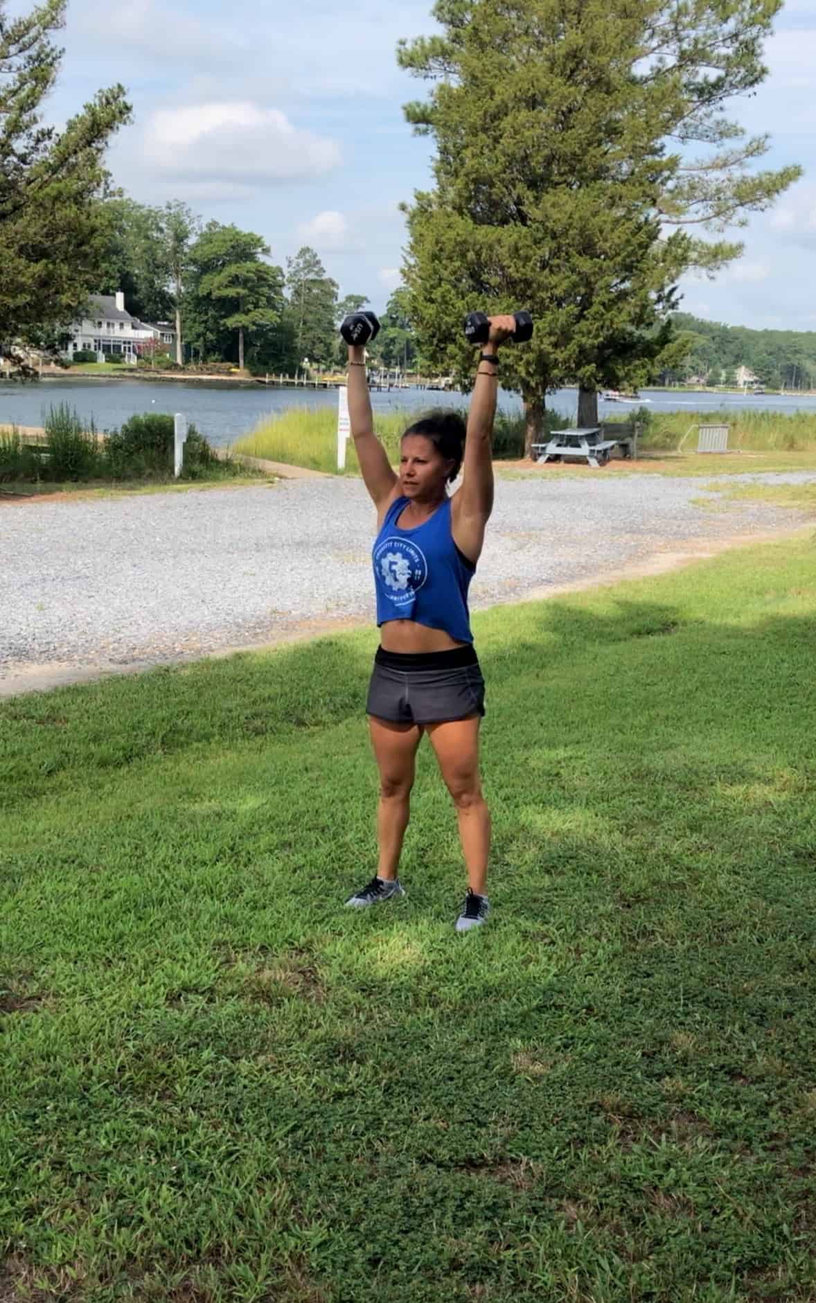 Girl doing an overhead press outside in the grass by the bay