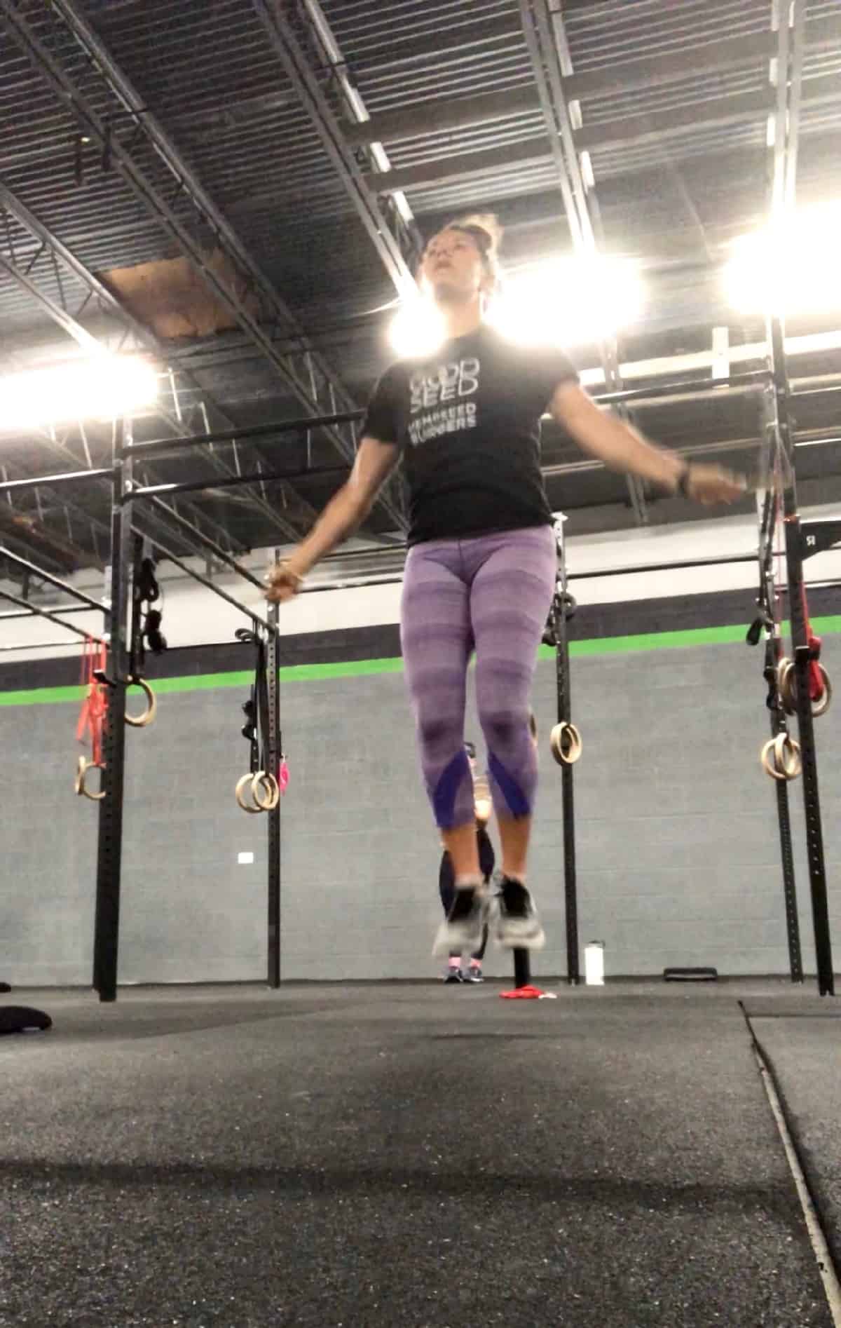 Girl in purple leggings and a tee shirt jumping rope in a CrossFit gym