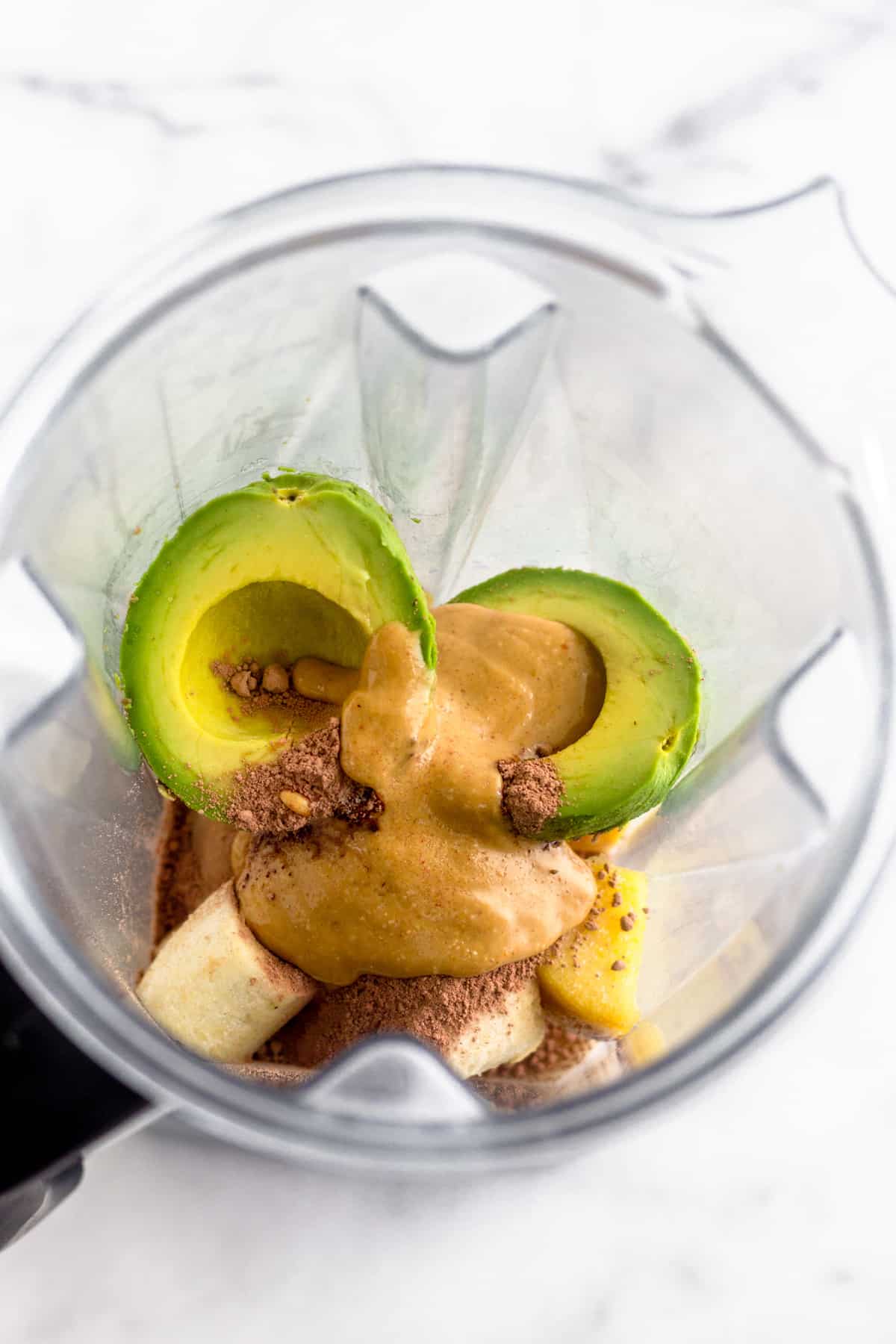 All the ingredients for a vegan peanut butter frosty in a Vitamix on a white counter