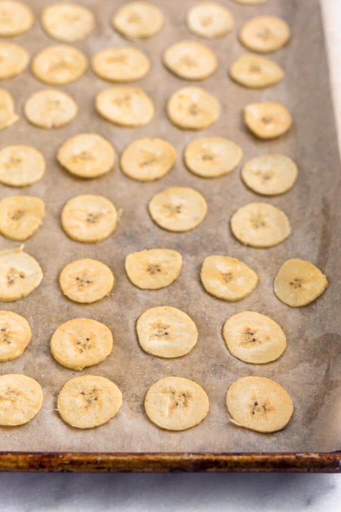 Thinly sliced plantain rounds on a baking sheet.