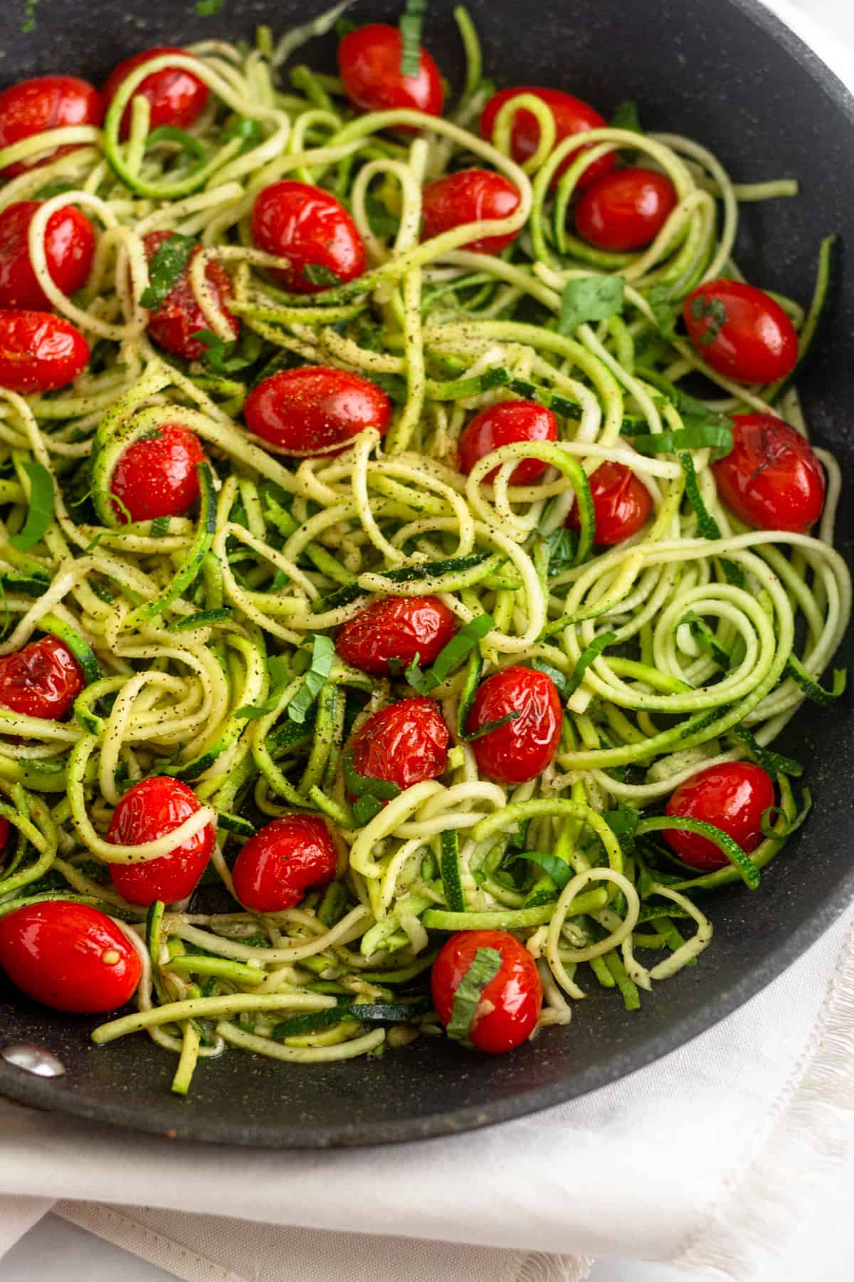 Large saute pan filled with zucchini noodles, blistered tomatoes, and fresh basil