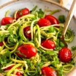 Bowl of zucchini noodles with blistered tomatoes and basil with a fork in it and a stick of butter behind it