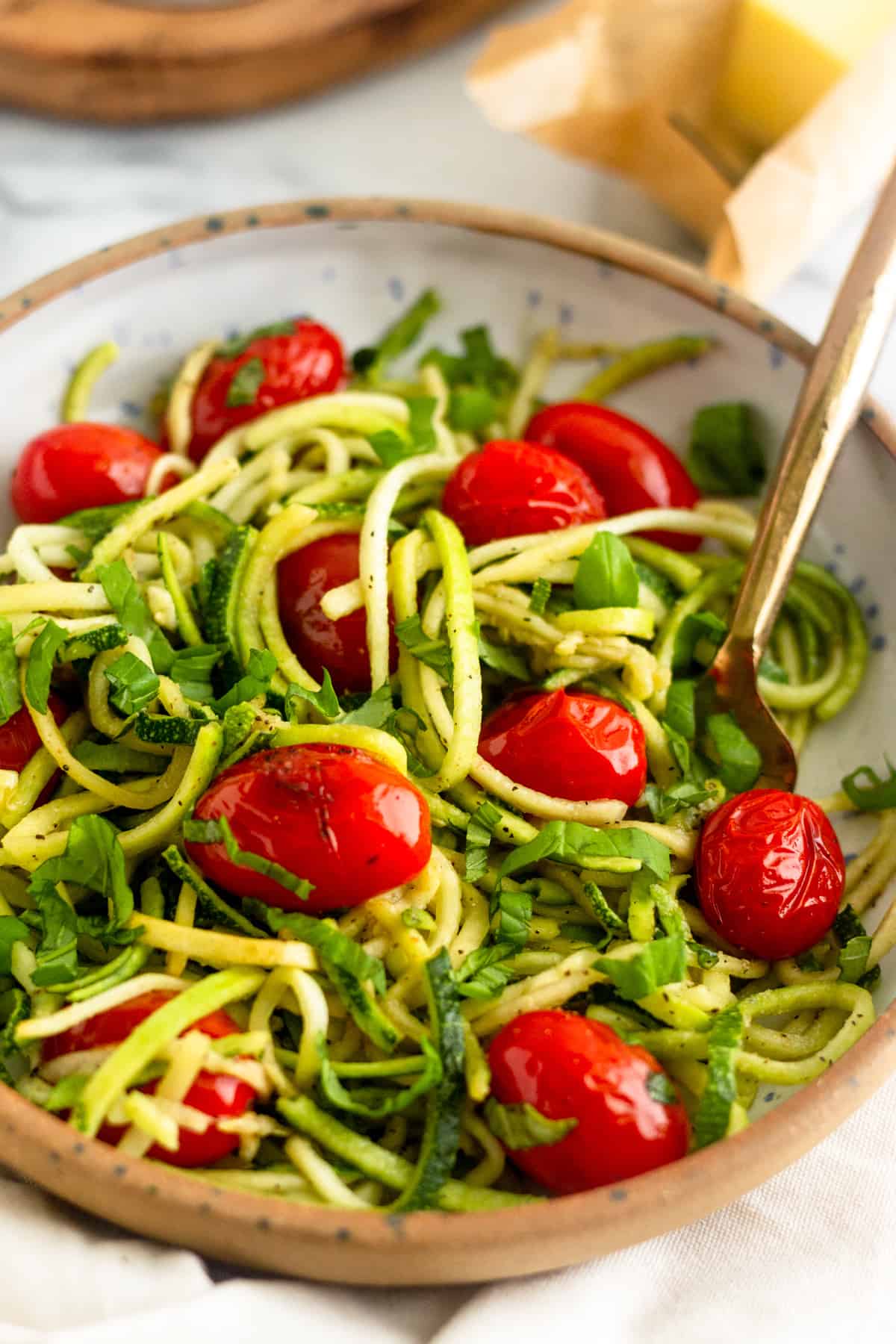 Bowl of zucchini noodles with blistered tomatoes and basil with a fork in it and a stick of butter behind it
