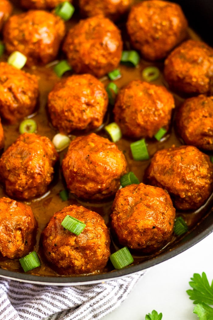 Close up of Whole30 BBQ chicken meatballs in a cast iron covered in bbq sauce and topped with green onions.
