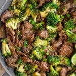 Healthy beef and broccoli stir fry in large skillet. It is topped with sesame seeds, green onion, and red pepper flakes.