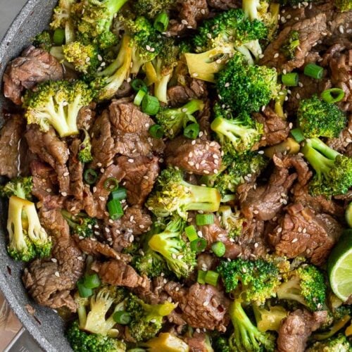 Healthy beef and broccoli stir fry in large skillet. It is topped with sesame seeds, green onion, and red pepper flakes.