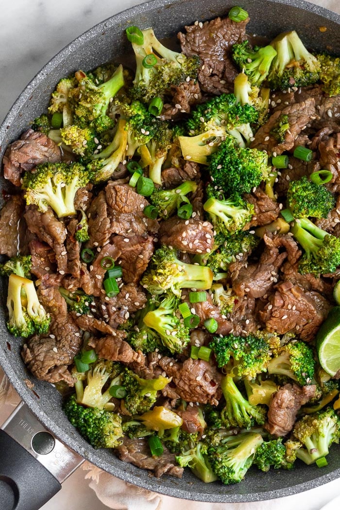 Healthy beef and broccoli stir fry in large skillet. It is topped with sesame seeds, green onion, and red pepper flakes.