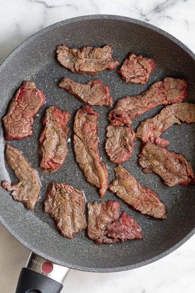 Large skillet with cooked thinly sliced flank steak in it.
