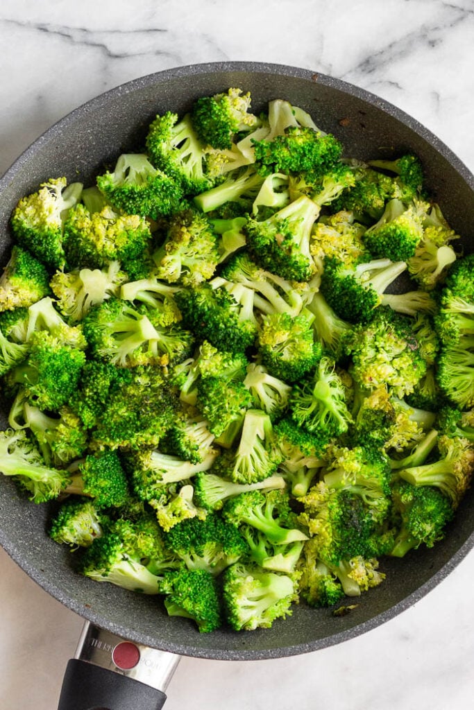 Large skillet with cooked broccoli in it.