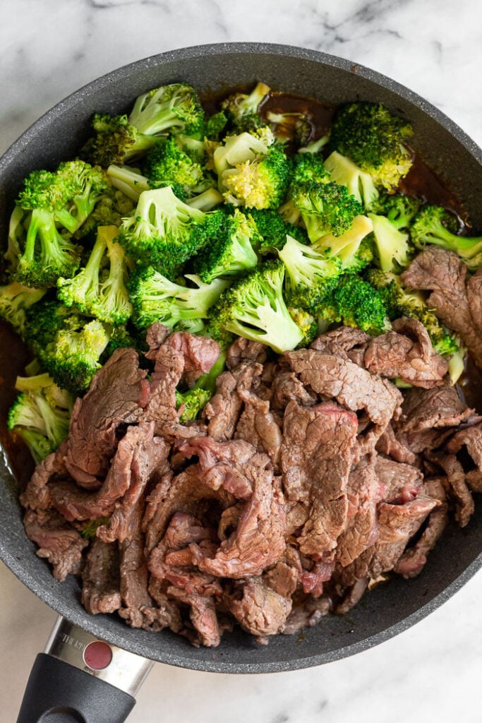 Large skillet with cooked broccoli and cooked steak top on of beef and broccoli sauce before it is mixed together.
