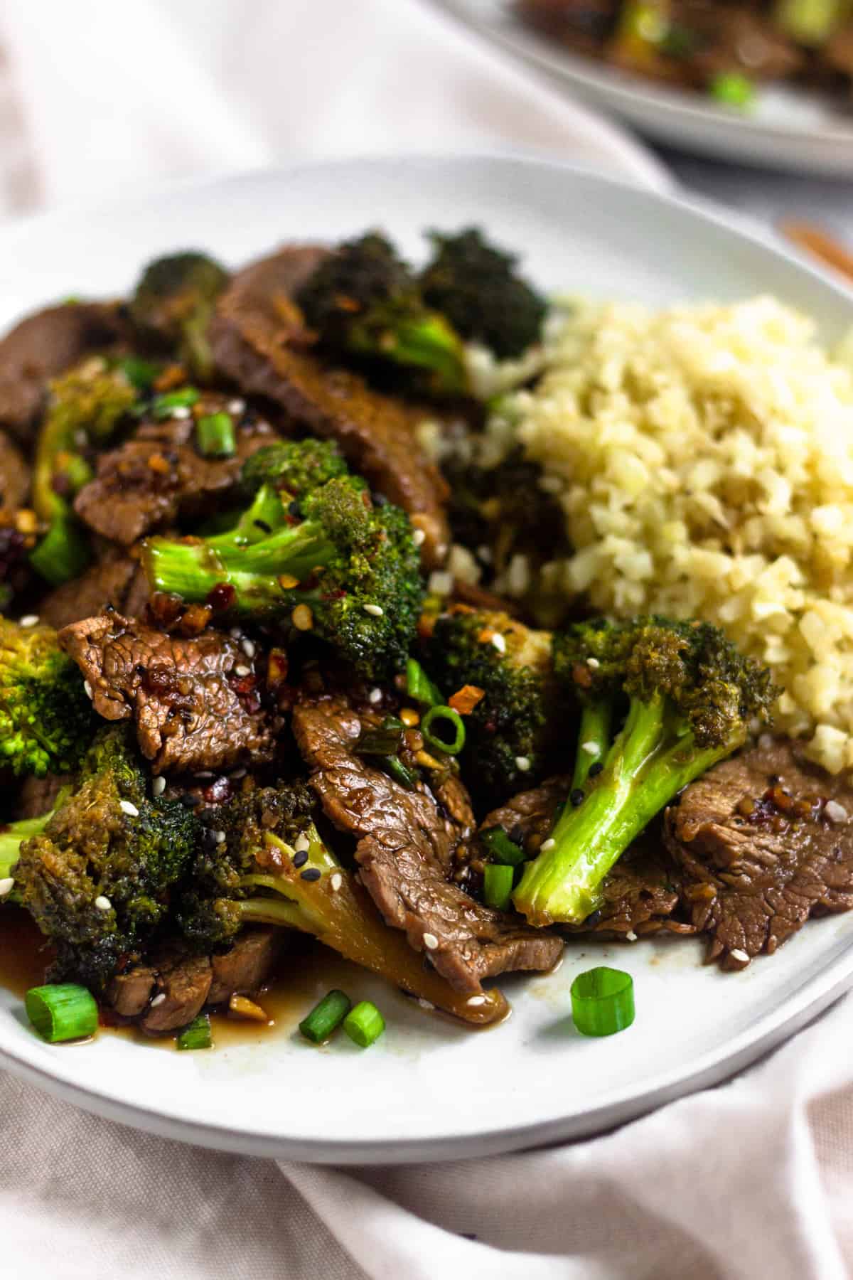 Close up of a plate of paleo beef & broccoli on a white plate on top of a white linen