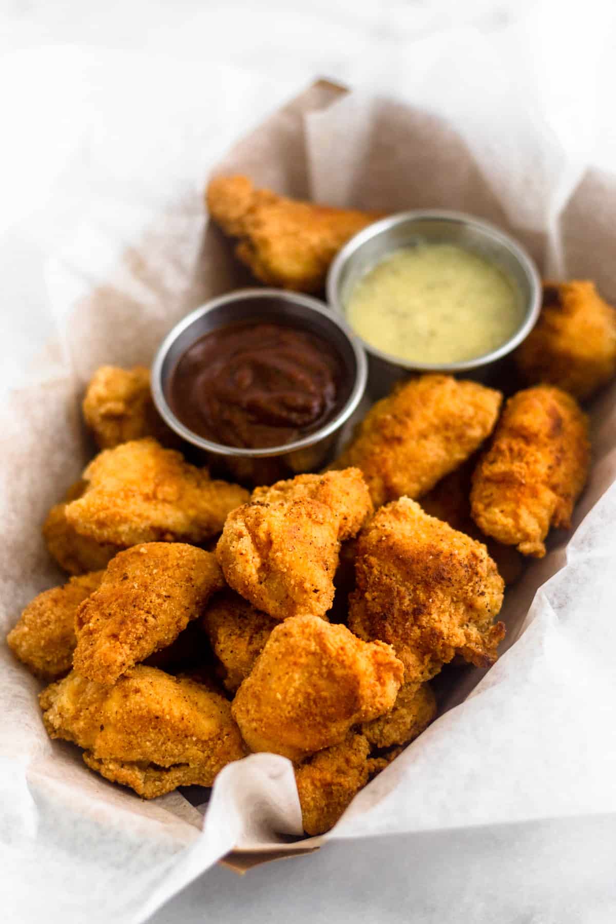 Basket of Whole30 and paleo popcorn chicken with two dipping sauces, one of BBQ and one of ranch