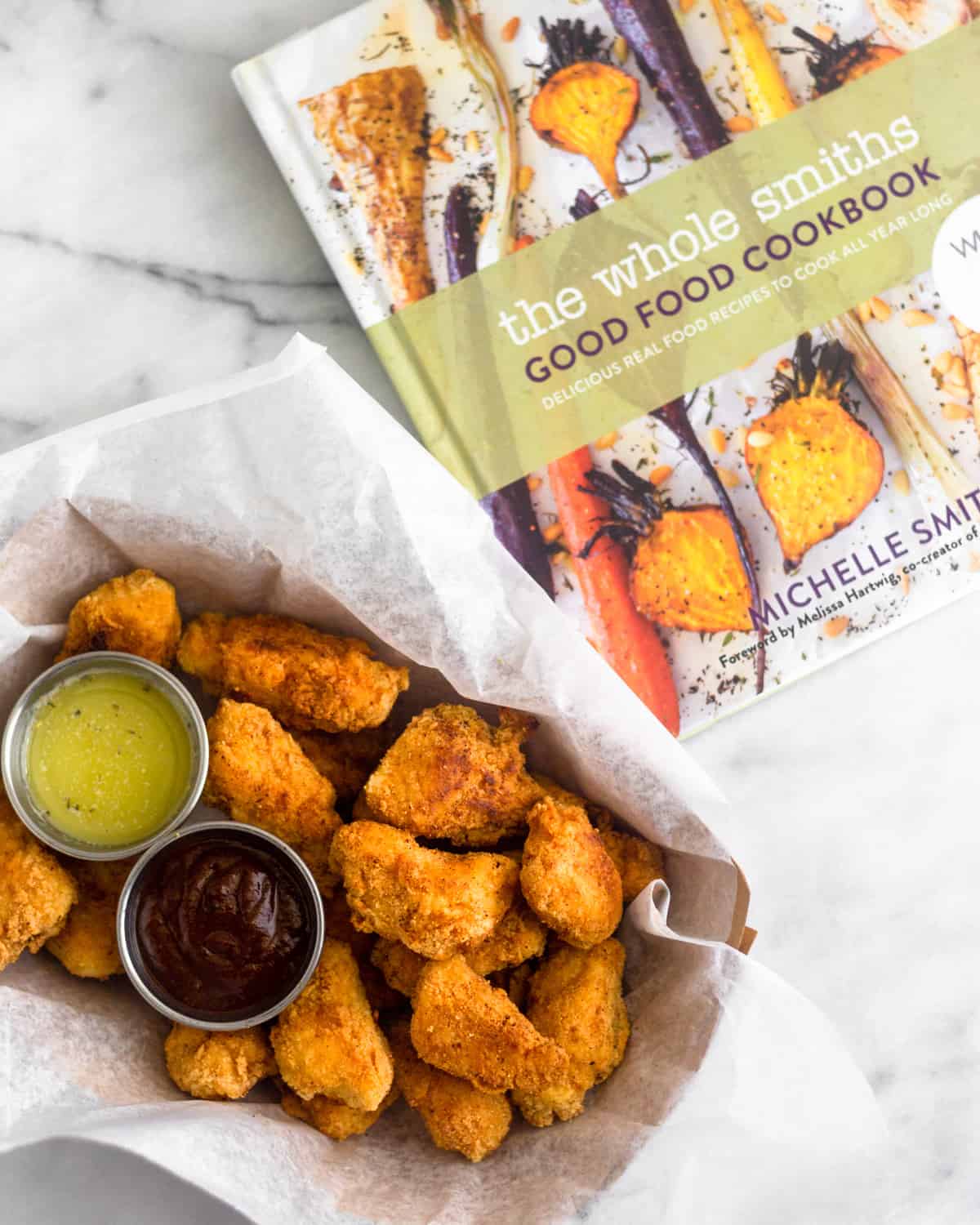 Basket of paleo popcorn chicken and two dipping sauces next to a Whole30 cookbook