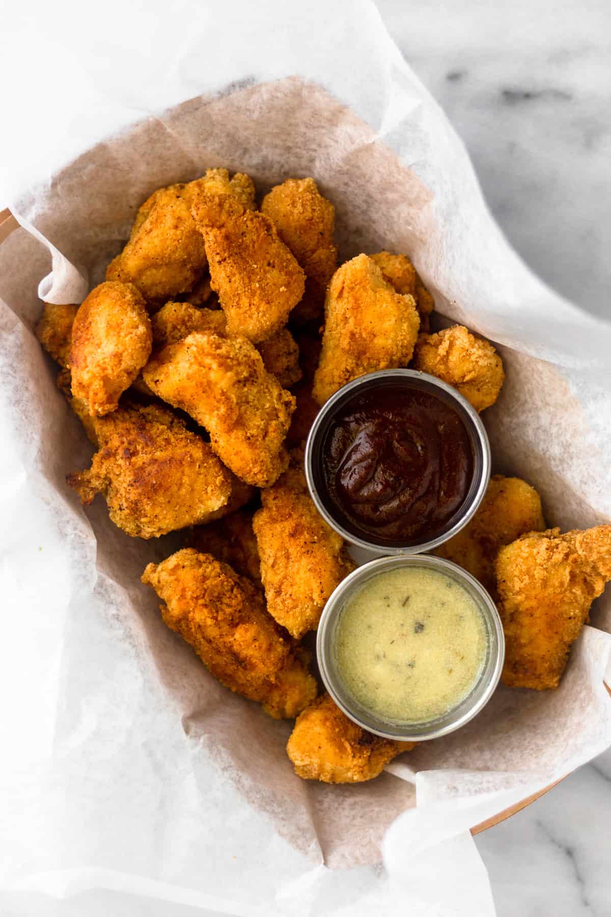 Overhead shot of a basket of paleo popcorn chicken with a cup of BBQ sauce and a cup of ranch in the basket