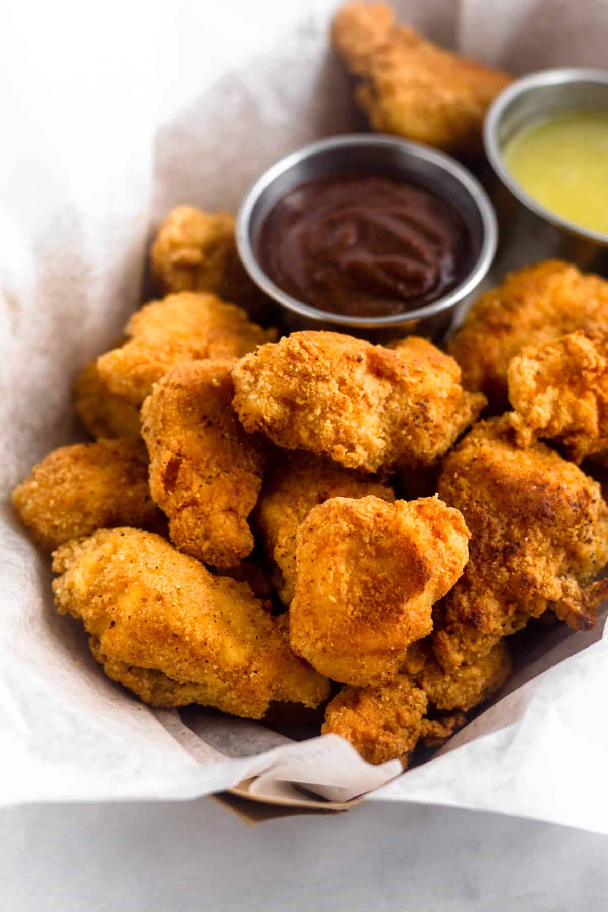 Close up of paleo popcorn chicken that is Whole30 and grain free. It is sitting in a cardboard basket with dipping sauces next to it