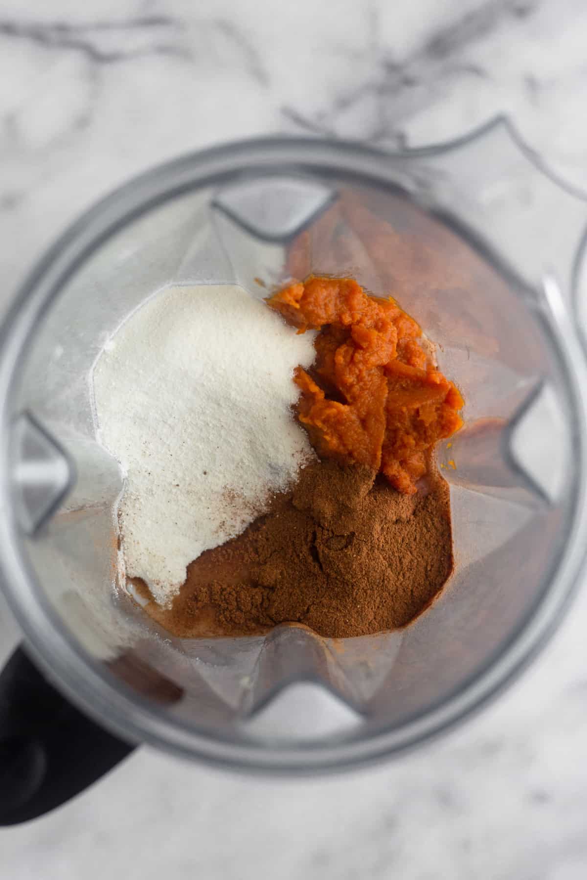 Blender filled with cashews, cashew milk, pumpkin, collagen, maple syrup, and pumpkin pie spice before it is going to blended for paleo pumpkin ice cream