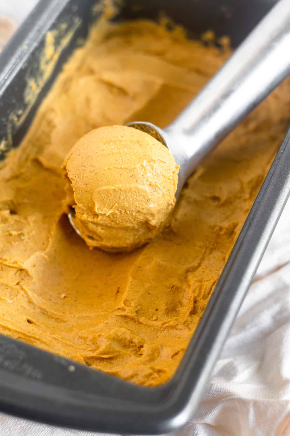 Bread pan filled with paleo pumpkin ice cream with an ice cream scoop filled with a scoop of pumpkin ice cream in it.