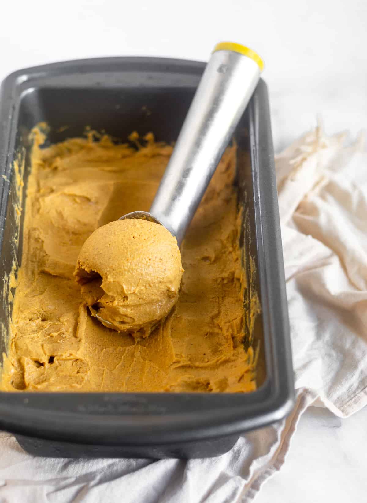 Small bread pan filled with dairy free and paleo pumpkin pie ice cream with a scoop of ice cream in an ice cream scooper in it.