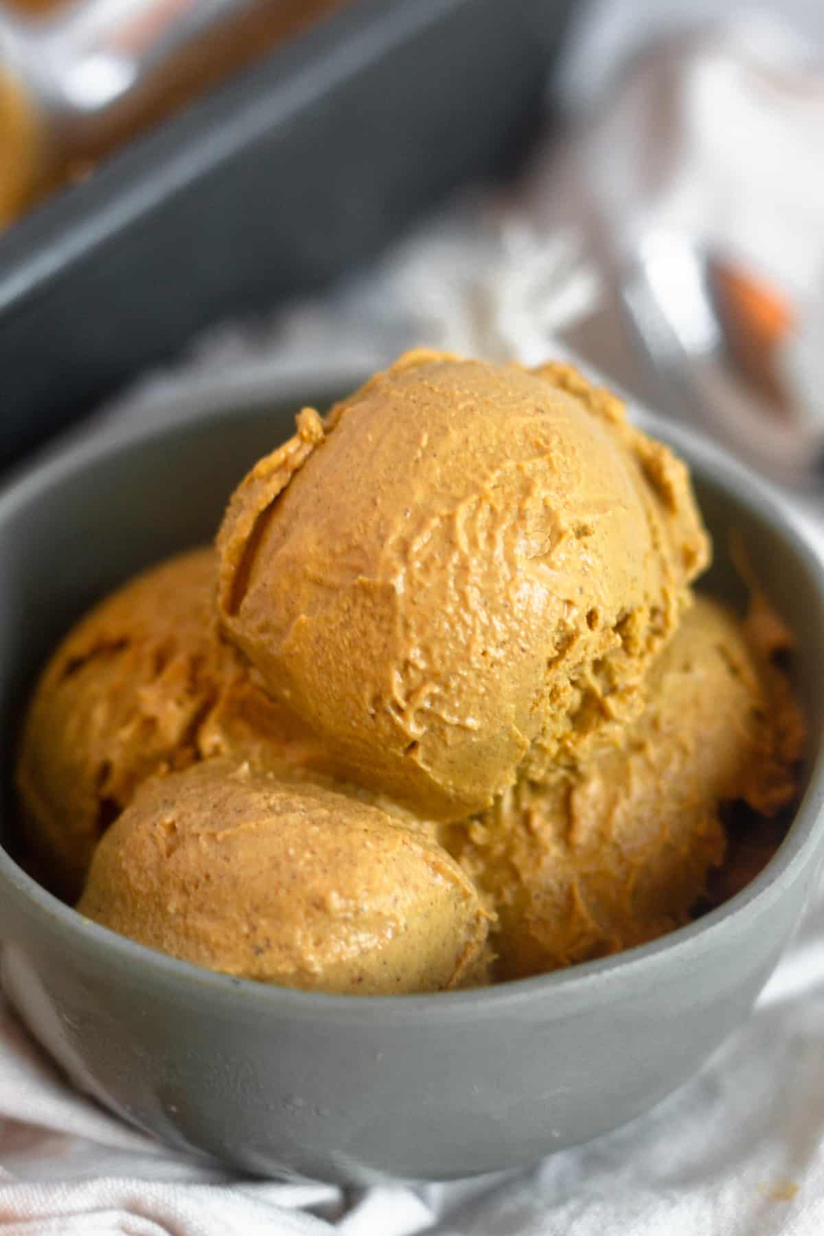 Small green bowl filled with dairy free paleo pumpkin ice cream sitting on a tan linen