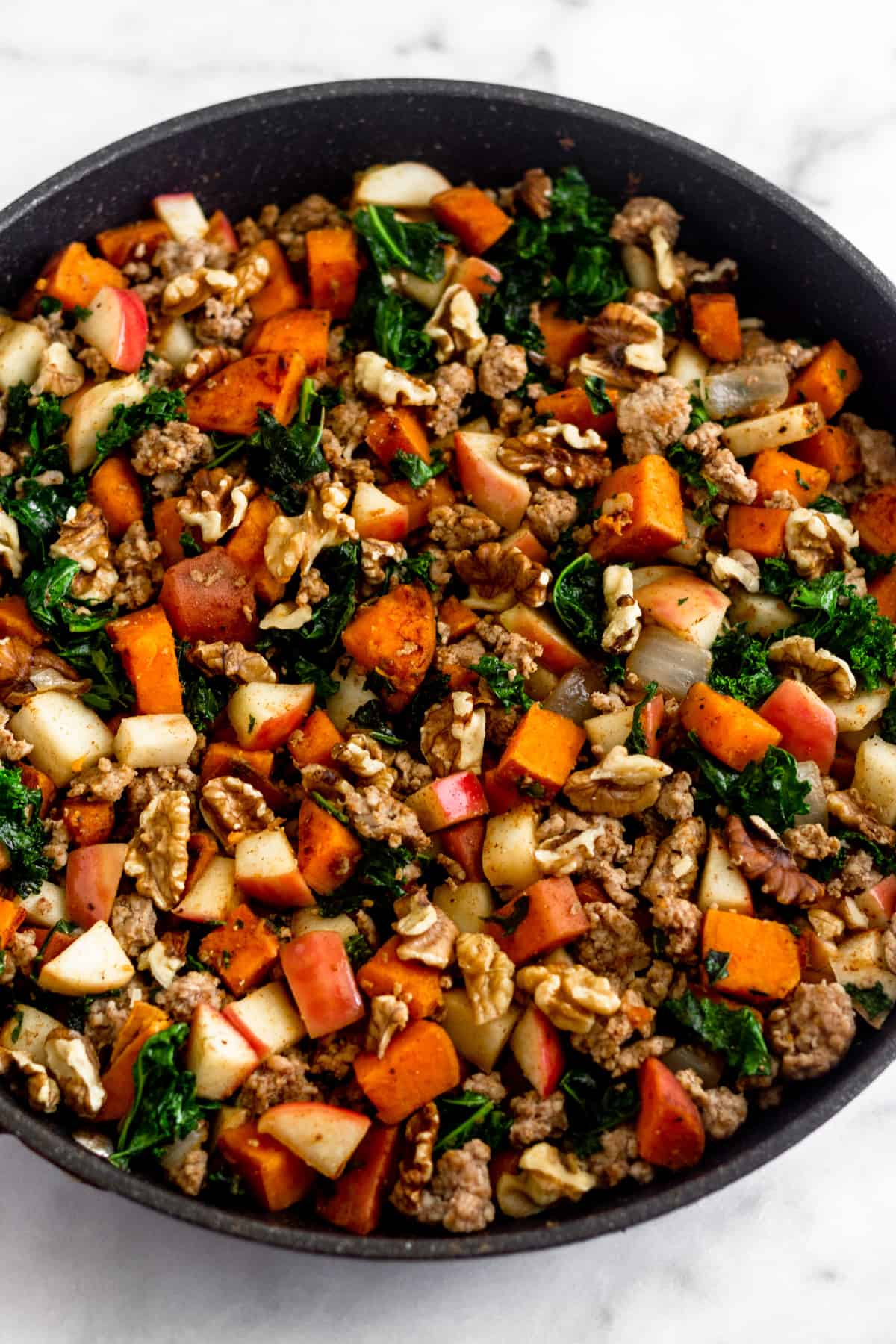 Large saute skillet filled with sweet potatoes, sausage, apples, kale, onions, and walnuts.