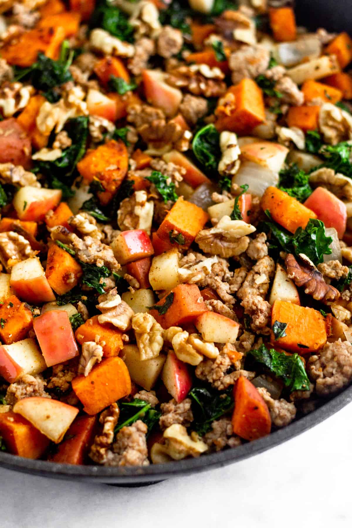 Close up of a large saute pan of of ground pork, sweet potatoes, kale, apples, and walnuts.