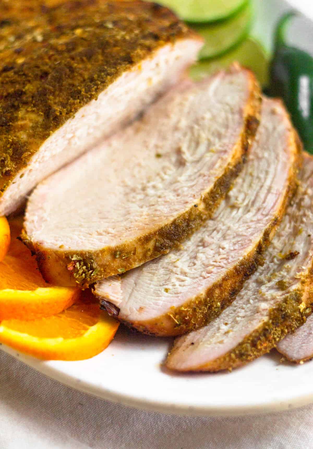 Close up of sliced citrus grilled turkey breast on a white platter next to sliced citrus