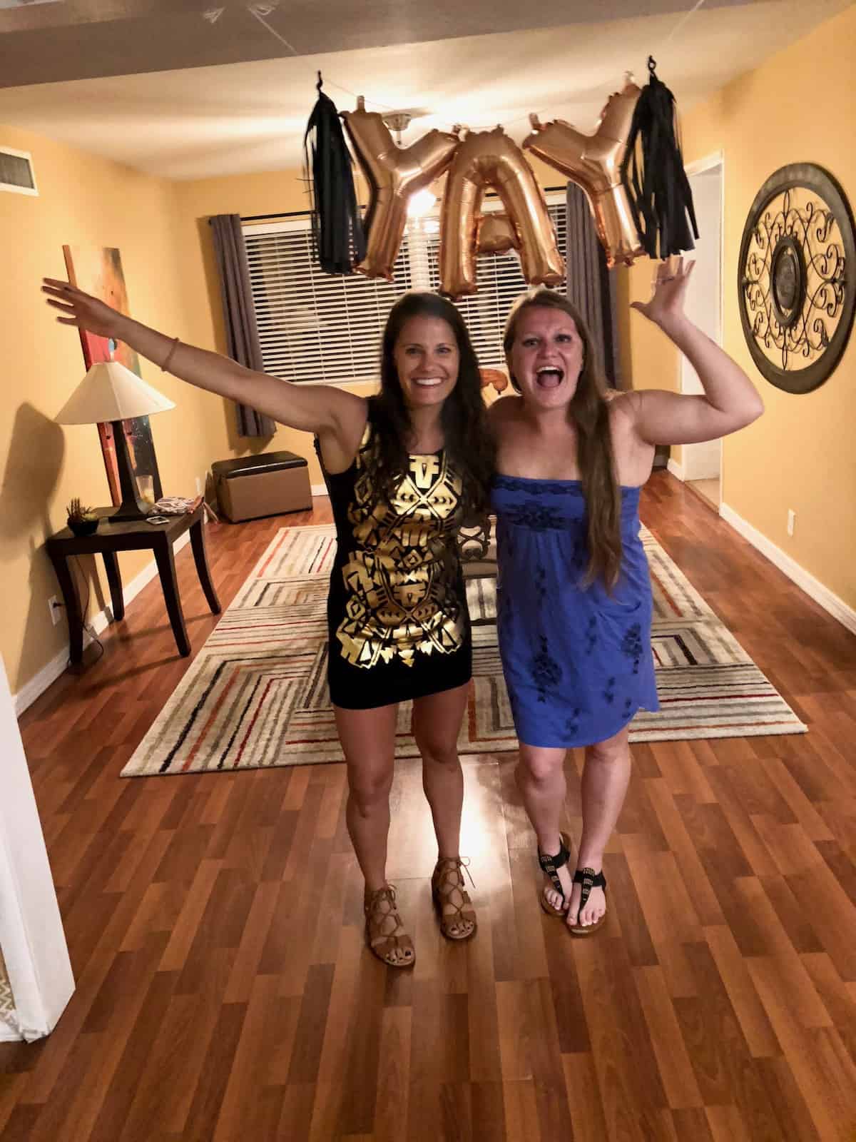 Two sisters dressed up in front of a balloons that say YAY