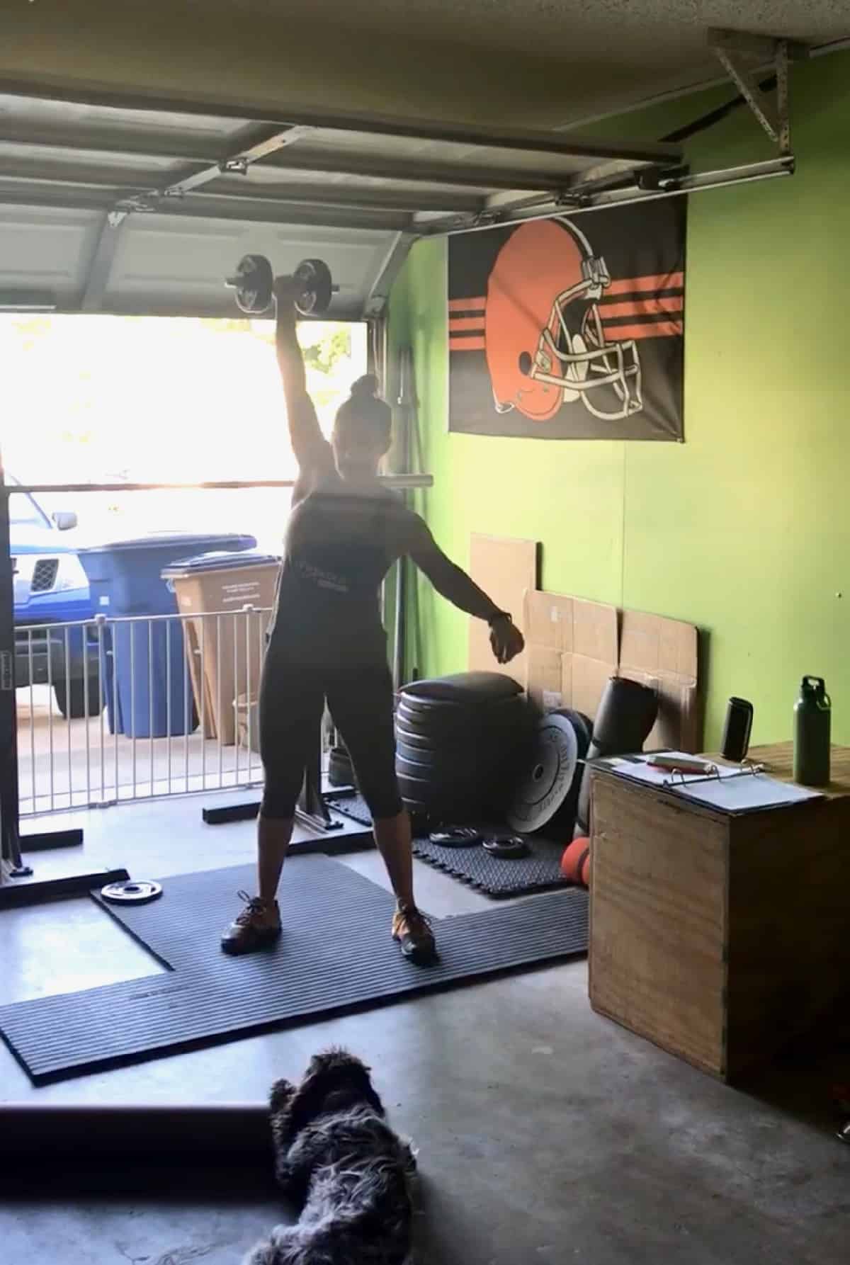 Girl in a garage gym doing a one arm dumbbell snatch