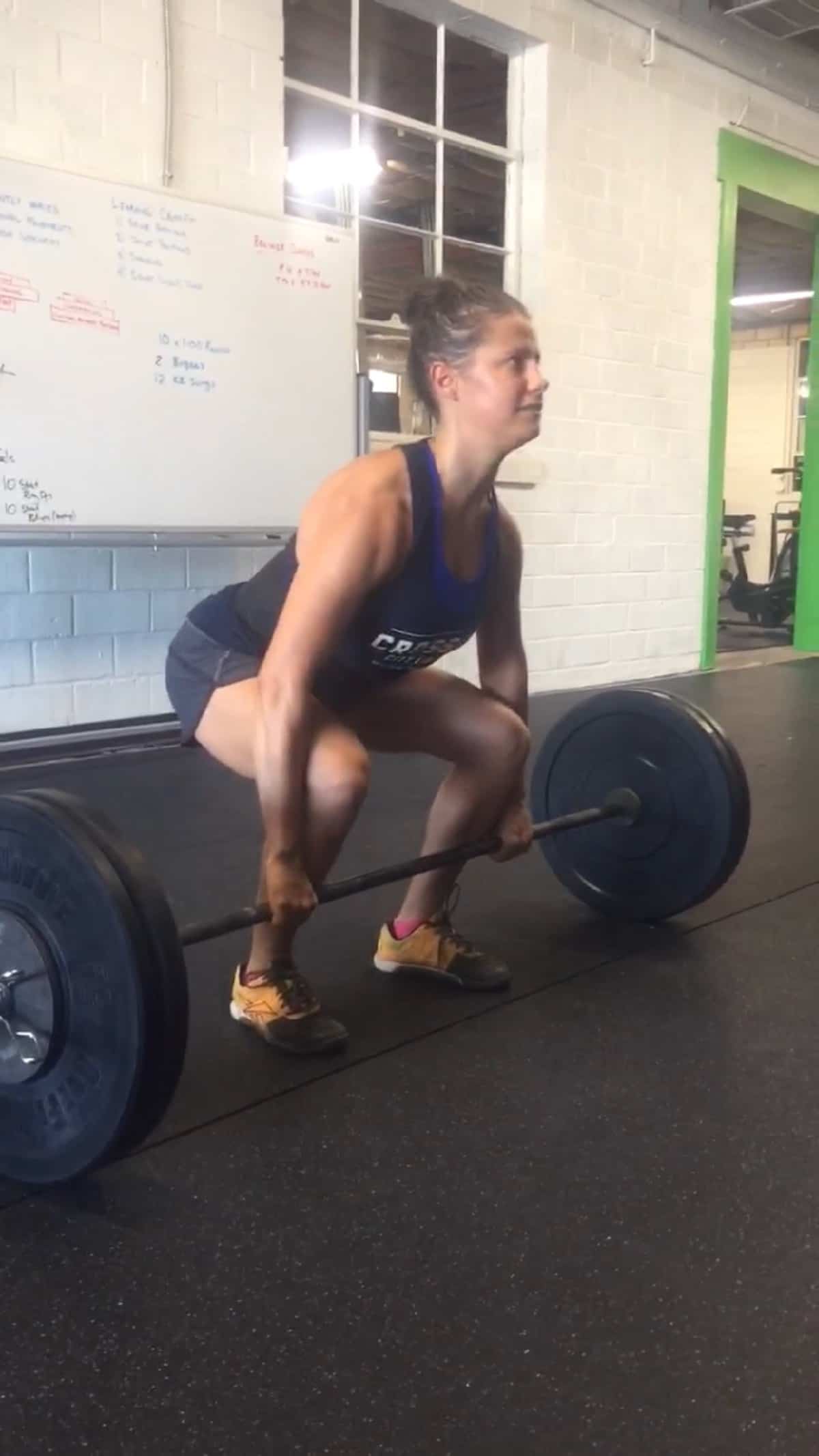 Girl squatting and holding onto a barbell about to do a power clean in a CrossFit gym