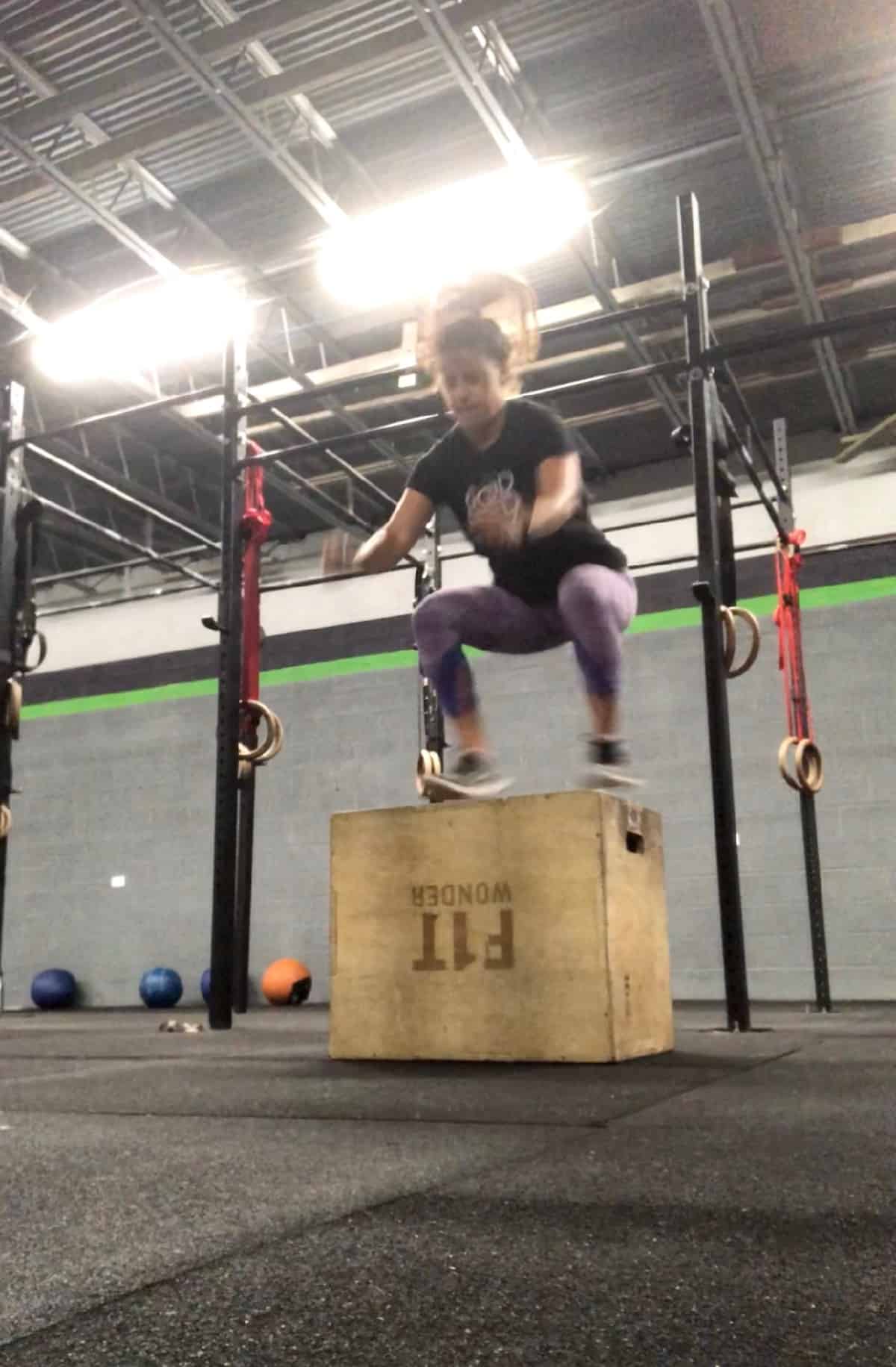 Girl jumping up onto a wooden box doing a box jump