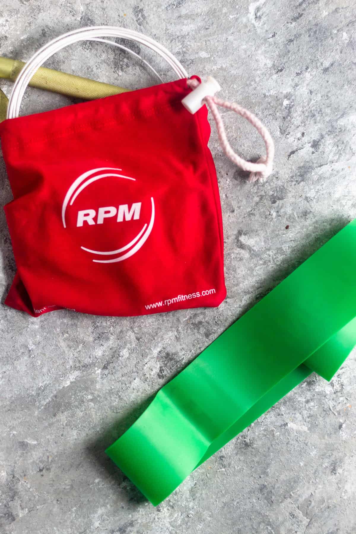 A jump rope in a small red bag and a green resistance band on a grey surface
